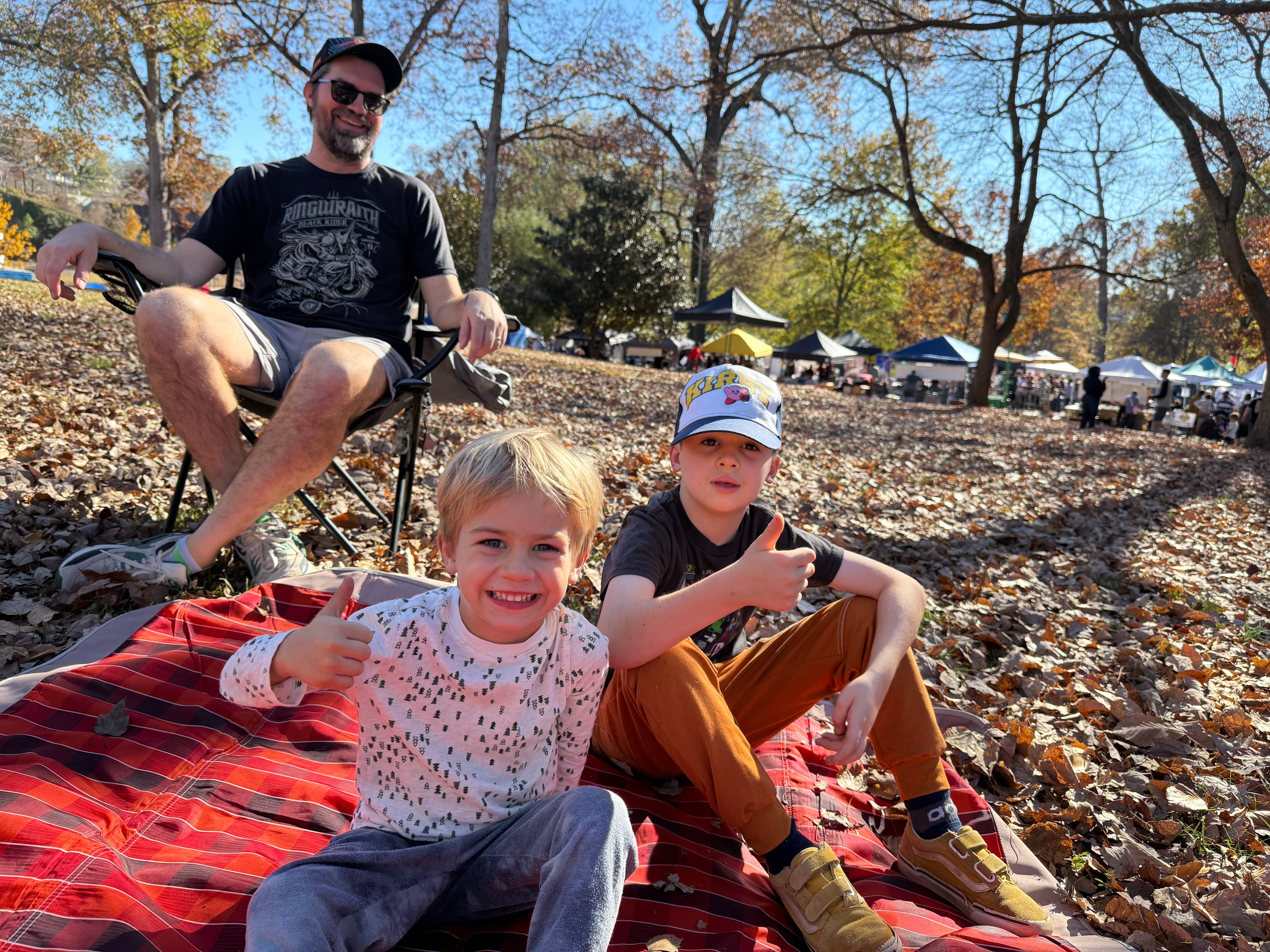 Matt Mastin, left, and his sons Arthur, center, and Oscar, right, give a thumbs up to the food at the Atlanta Halal Fall Festival, seen in Grant Park behind them on November 23, 2025. Photo by Ariel Hart ahart@ajc.com
