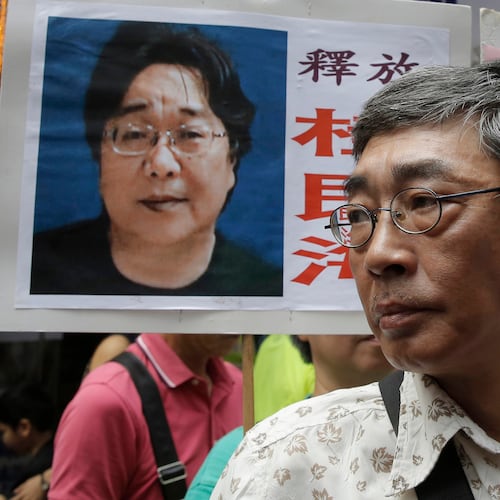 FILE - Freed Hong Kong bookseller Lam Wing-kee stands next to a placard with a picture of missing bookseller Gui Minhai, left, in front of his book store during a march in Hong Kong on June 18, 2016. (AP Photo/Kin Cheung, File)
