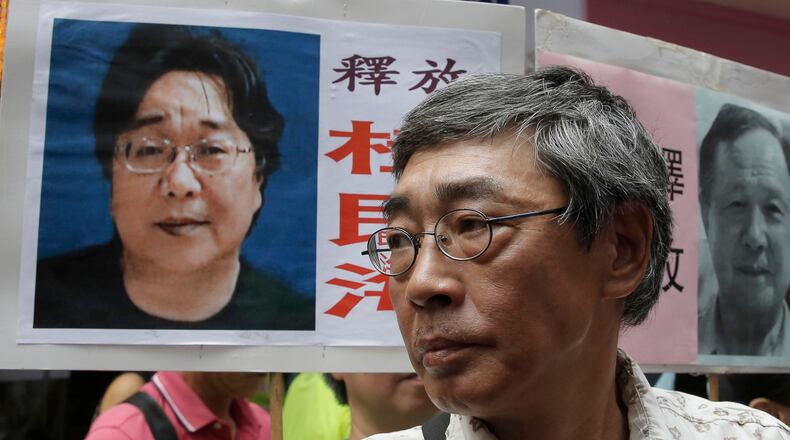 FILE - Freed Hong Kong bookseller Lam Wing-kee stands next to a placard with a picture of missing bookseller Gui Minhai, left, in front of his book store during a march in Hong Kong on June 18, 2016. (AP Photo/Kin Cheung, File)
