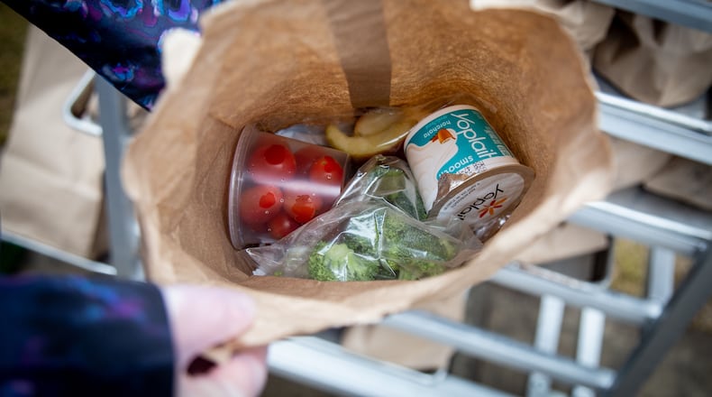 Lilburn Elementary School office worker Lucy Torp holds one of the free lunches that was given out to anyone under 18 on March 16. Gwinnett County and Gwinnett County Public Schools are teaming up to help ease hardships during the COVID-19 pandemic by continuing to feed Gwinnett’s children during the summer. STEVE SCHAEFER / SPECIAL TO THE AJC