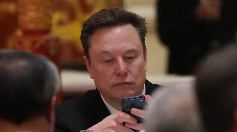 FILE - Elon Musk uses his phone during a state dinner for President Donald Trump and Chinese President Xi Jinping at the Great Hall of the People on Thursday May 14, 2026, in Beijing. (AP Photo/Mark Schiefelbein, File)
