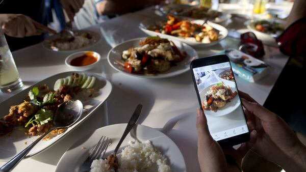In this Dec. 20, 2017, photo, a customer takes photos of food cooked by Thai cook Supinya Jansuta, 72, better known as "Jay Fai,"  at her eatery in Bangkok, Thailand. After spending more than three decades cooking in an unassuming outdoor kitchen, Jay Fay has been propelled to international culinary stardom by having her restaurant awarded a Michelin star. (AP Photo/Gemunu Amarasinghe)