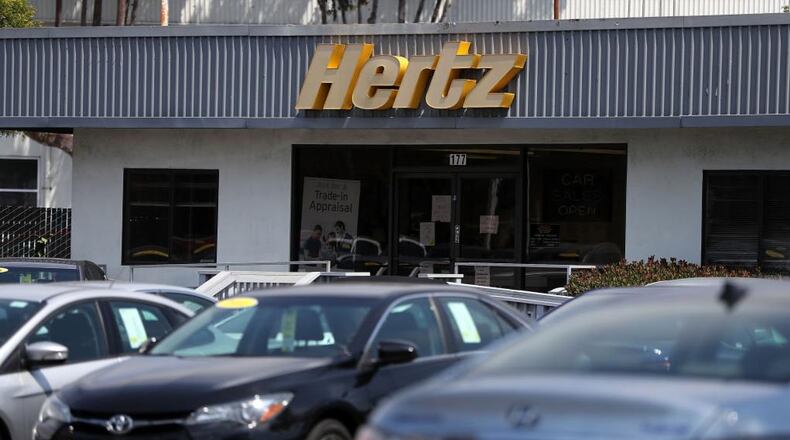 A sign is posted in front of a Hertz sales and rental car office.