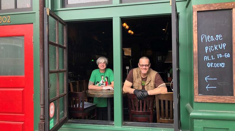 Manager John Gore (left) and co-owner Phil Roness of Meehan’s Public House in Vinings await food to go customers, as the restaurant’s dining room is closed due to the COVID-19 outbreak. Forsyth County similarly has prohibited indoor dining at restaurants. AJC FILE