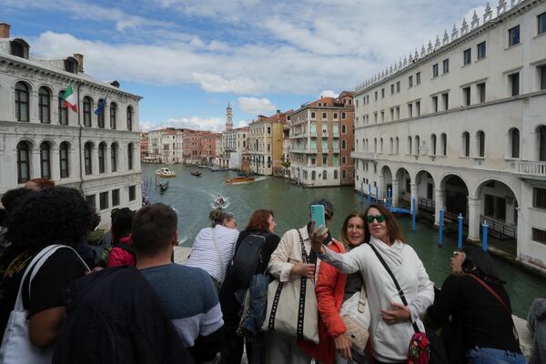 Tourists take pictures on Rialto Bridge "Ponte di Rialto" in Venice, Italy, Friday, April 18, 2025, Venice on Friday launches for a second year a pilot program to charge day-trippers an entrance fee. (AP Photo/Antonio Calanni)