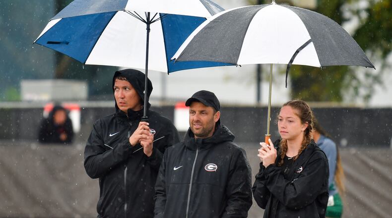 Georgia coach Petro Kyprianou (center) finds some relief from the rain under the umbrellas of a couple of track team members during the Spec Towns Invitational at the Spec Towns Track in Athens on Saturday, April 10, 2021. (Photo by Rob Davis/UGA Athletics)