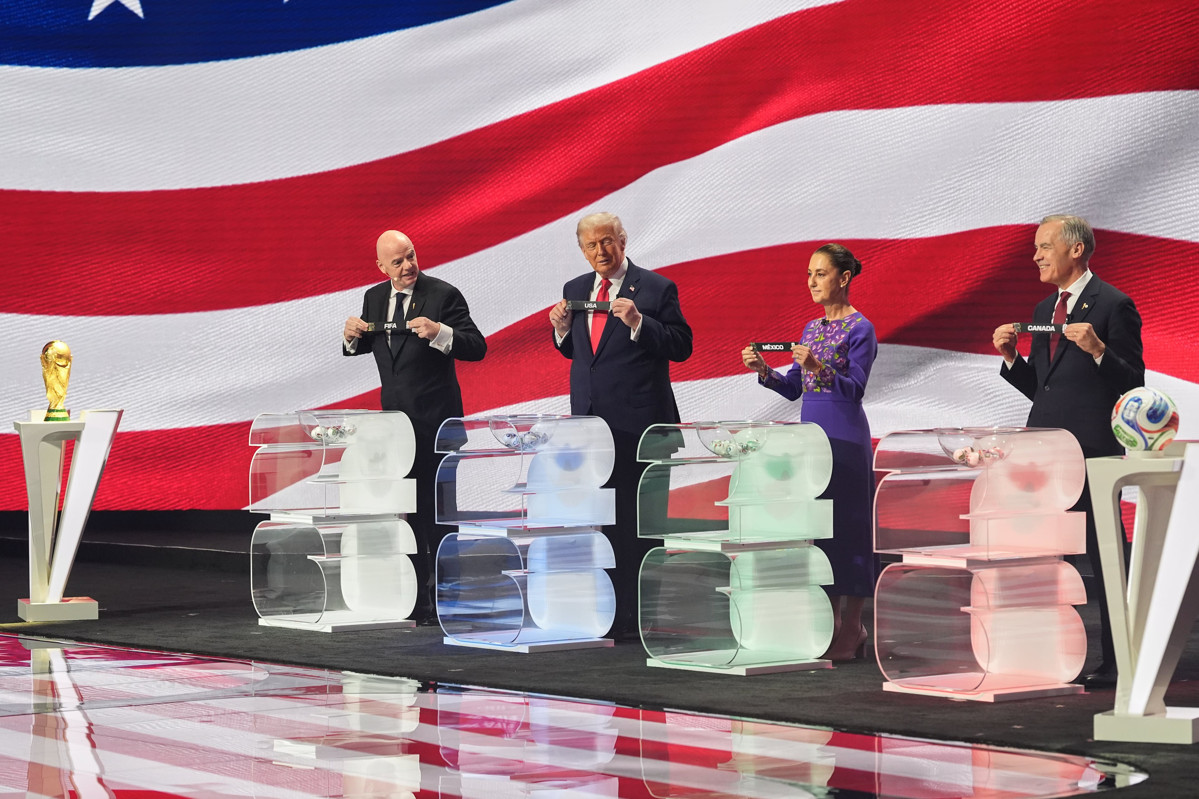 Canadian Prime Minister Mark Carney, Mexican President Claudia Sheinbaum, President Donald Trump and FIFA President Gianni Infantino hold up country names during the draw for the 2026 soccer World Cup at the Kennedy Center in Washington, Friday, Dec. 5, 2025. (AP Photo/Jacquelyn Martin)