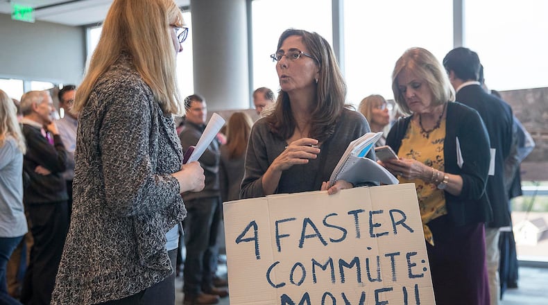 Sandy Springs resident Malia Jeffers holds a sign of protest while speaking with a GDOT project consultant during a GDOT open house meeting with North Fulton residents at the Sandy Springs City Hall in Sandy Springs, Tuesday, March 12, 2019. (ALYSSA POINTER/ALYSSA.POINTER@AJC.COM)