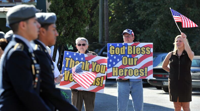 Lee Webb (background left), of Marietta, and Tim Spaeth, of Roswell, hold signs to show their support as Osborne High School JROTC members march along Roswell Street during the 10th annual Marietta Veterans Day Parade at Roswell Street Baptist Church in Marietta on Tuesday, November 11, 2014. HYOSUB SHIN / HSHIN@AJC.COM