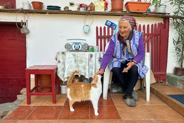 Zoica Roth, 83, pets her three-legged cat in the village of Saschiz, in Romania's central Transylvania region, Friday, April 25, 2025. (AP Photo/Stephen McGrath)