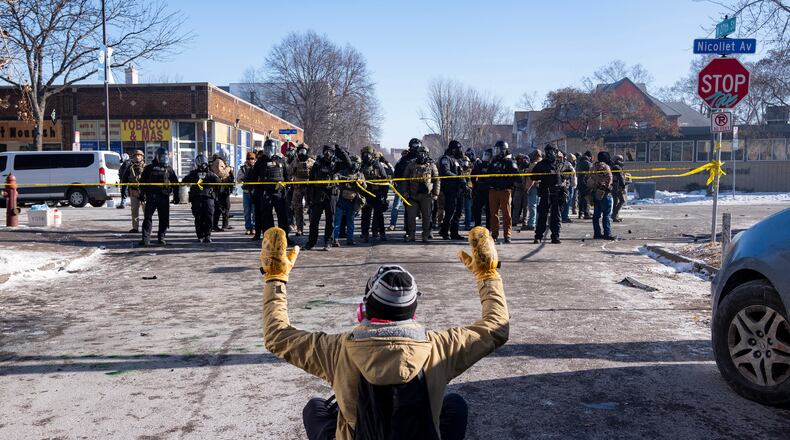 A protester sits on the street with his arms up in front of federal agents in Minneapolis, on Saturday, Jan. 24, 2026. (Alex Kormann/Star Tribune via AP)