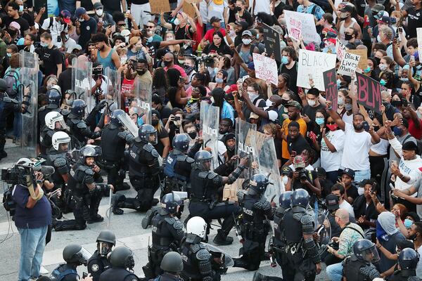 In a show of peace and solidarity, law enforcement officials with riot shields take a knee before protesters during a fourth day of protests on Monday, June 1, 2020, in Atlanta. 