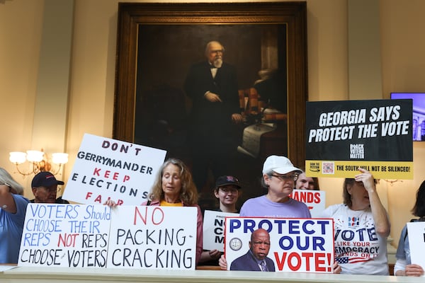 Activists opposed to redistricting hold signs in front of a painting of Reconstruction-era Governor Charles Jenkins at a press conference before the state legislature convenes for a special session in Atlanta on June 17, 2026. Georgia Republican leaders later announced that they wouldn’t redraw the state’s political maps during the session. (Arvin Temkar/AJC)