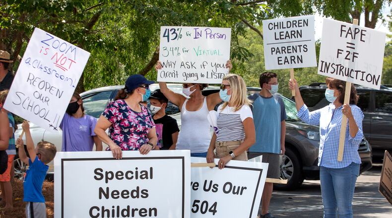 Michelle Russell, left, and Stacey Dickinson, center, hold signs supporting special needs children during a demonstration at the Gwinnett Instructional Support Center in Suwanee on July 27. STEVE SCHAEFER FOR THE ATLANTA JOURNAL-CONSTITUTION