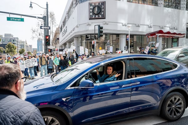 A Tesla driver shrugs while passing protesters against Tesla CEO Elon Musk in San Francisco on Saturday, March 29, 2025. (AP Photo/Noah Berger)