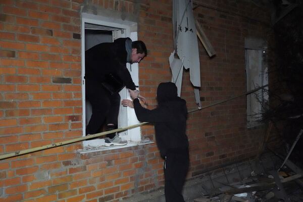 People walk out though a window of a house destroyed in a Russian strike on a residential neighborhood of Kharkiv, Ukraine, Saturday, March 29, 2025. (AP Photo/Andrii Marienko)