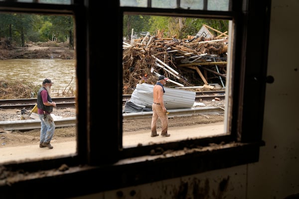 FILE - People walk by a pile of debris left in the wake of Hurricane Helene, Oct. 1, 2024, in Marshall, N.C. (AP Photo/Jeff Roberson, File)