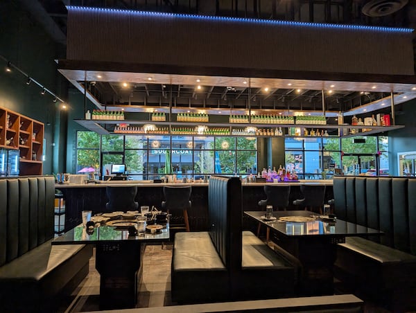 A view from inside a restaurant looking out towards large, exterior windows, with booth seating and bar in between the viewer and the windows.