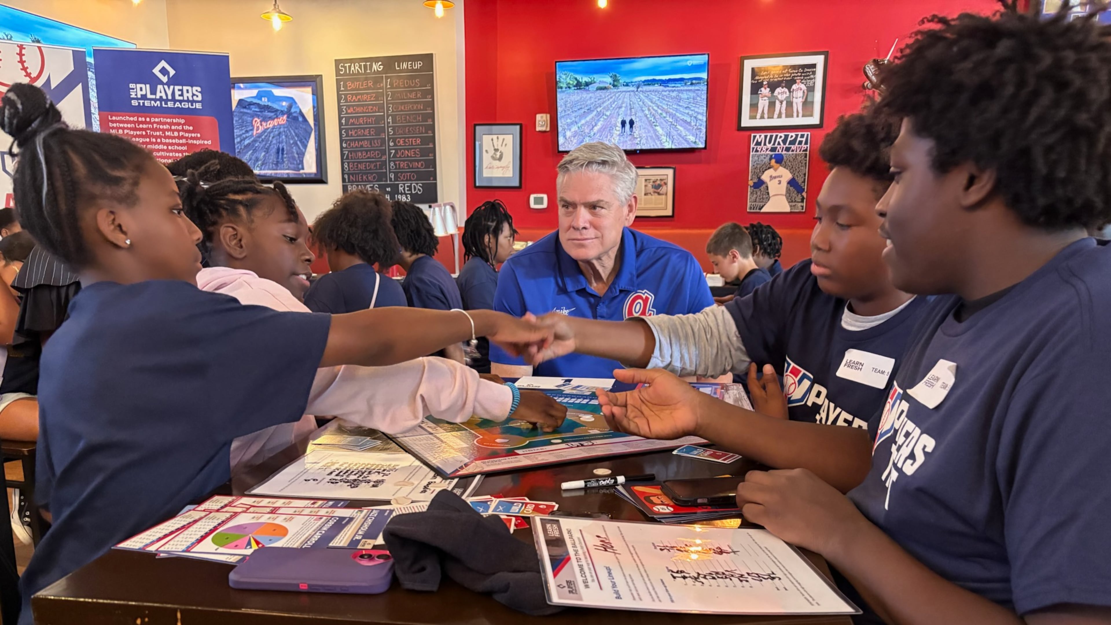 Braves legend Dale Murphy (center) watches four students in the Horizons Atlanta at Woodward Academy summer educational program play a math game involving baseball at Murph's restaurant at the Cobb Galleria in June. The students are, from left, Mariah Cunningham, Azaria Matthews (on Murphy's immediate right), Jeremiah Hindsman (Murphy's immediate left) and Jayvion Dickerson. The restaurant is set to close Tuesday, Aug. 12, 2025, because of renovations at the mall. (Ken Sugiura/AJC)