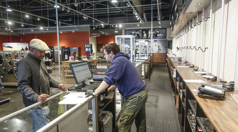Grahame Grantham (center), a manager at Stoddard’s Range and Guns in Atlanta, in front of an empty display wall, helps a customer wanting to make a purchase. The store has seen an uptick in ammunition and gun sales as the coronavirus threat intensifies. Bob Andres / robert.andres@ajc.com