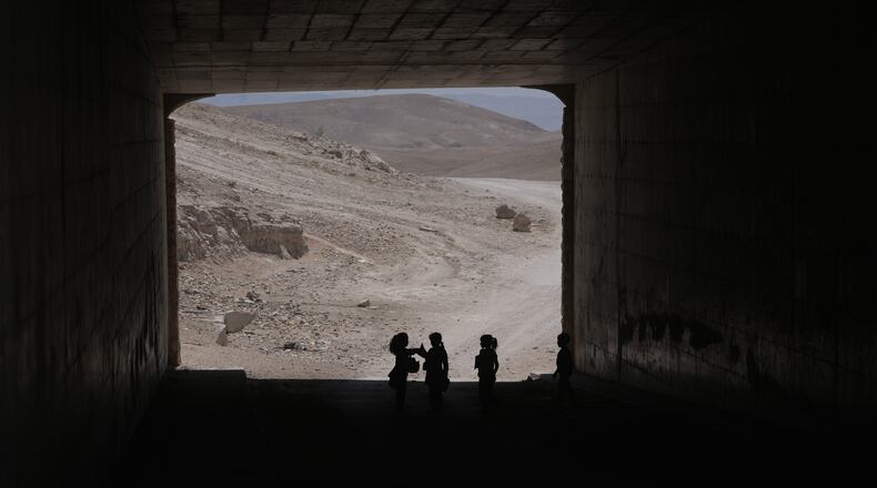 Palestinian children go through a vehicles tunnel on their way home, after receiving their year end reports from their school, in the West Bank Bedouin hamlets of Khan al-Ahmar, Wednesday, June 10, 2026. (AP Photo/Mahmoud Illean)