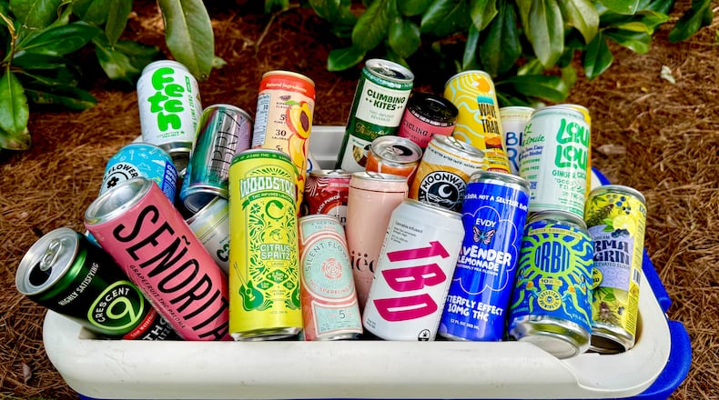 An open cooler is placed on the ground outside. It is overflowing with colorful cans of different cannabis-infused beverages.