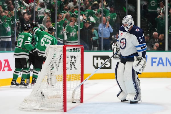 Winnipeg Jets goaltender Connor Hellebuyck reaches for the puck as the Dallas Stars celebrate a goal scored by Wyatt Johnston in the third period of Game 3 of a second-round NHL hockey playoff series in Dallas, Sunday, May 11, 2025. (AP Photo/Julio Cortez)