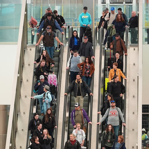 Travellers head down an escalator after clearing through a security checkpoint in Denver International Airport Friday, Nov. 7, 2025, in Denver. (AP Photo/David Zalubowski)