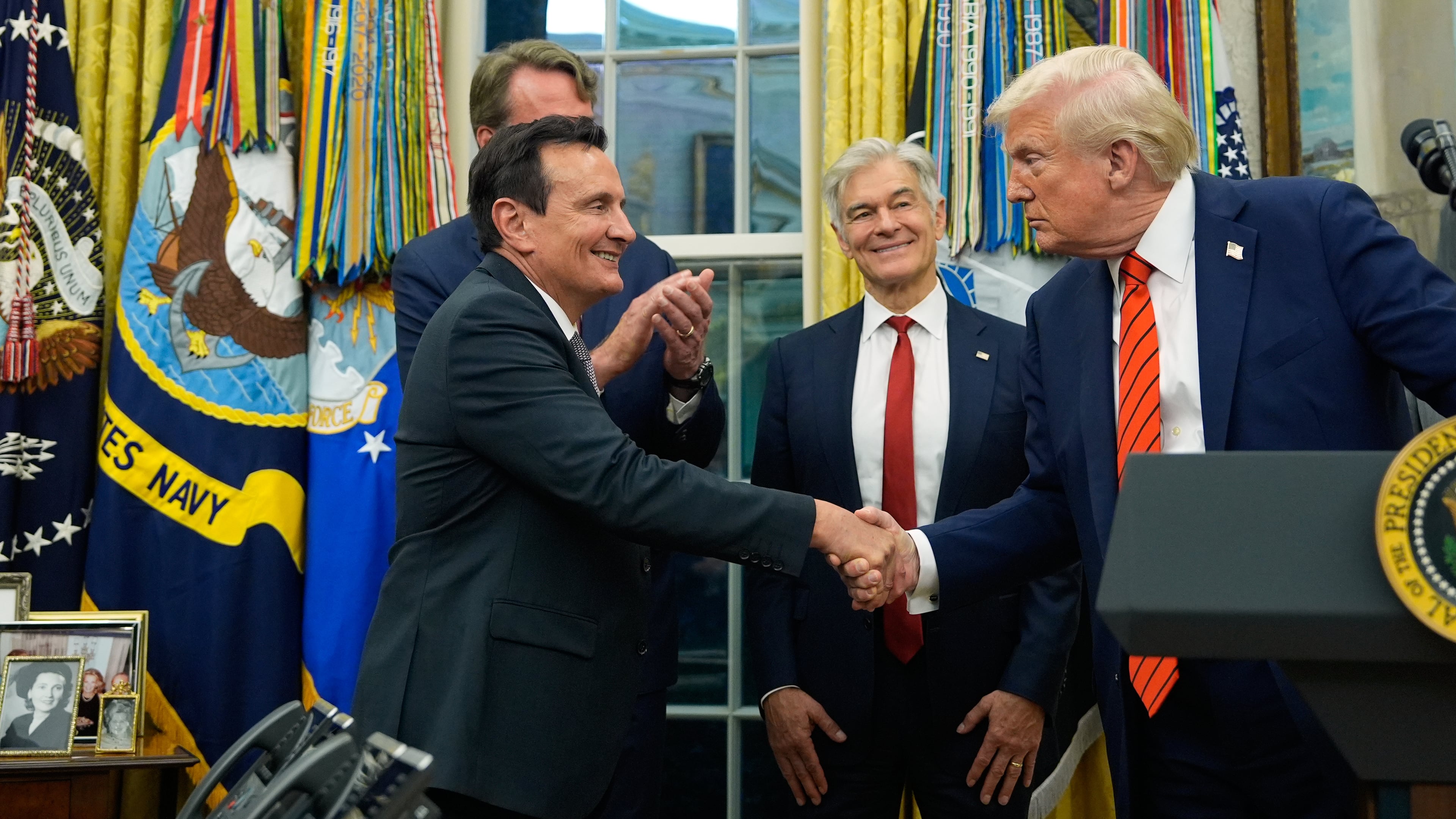 President Donald Trump shakes hands with AstraZeneca CEO Pascal Soriot in the Oval Office of the White House, Friday, Oct. 10, 2025, in Washington, as Virginia Gov. Glenn Youngkin and Centers for Medicare & Medicaid Services administrator Dr. Mehmet Oz watch. (AP Photo/Alex Brandon)