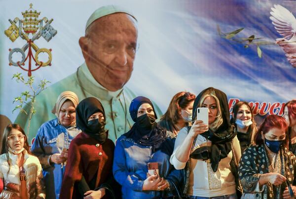 FILE.- Women wait outside the Chaldean Cathedral of Saint Joseph, in Baghdad, Iraq, Saturday, March 6, 2021, where Pope Francis, depicted on a giant poster at their back, is concelebrating a mass. (AP Photo/Andrew Medichini,File)
