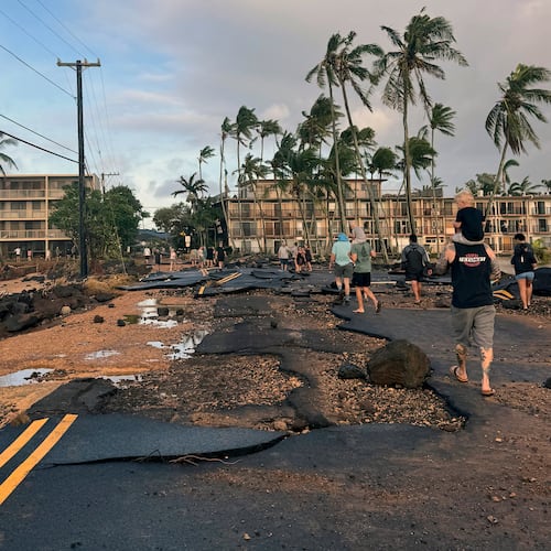 This photo taken with a smartphone, People walk past damage caused by Hurricane Lowell on Tuesday, Sept. 8, 2026 in Poʻipū on Kauaʻi's south shore, in Hawaii. (Guy Miller/Honolulu Civil Beat via AP)