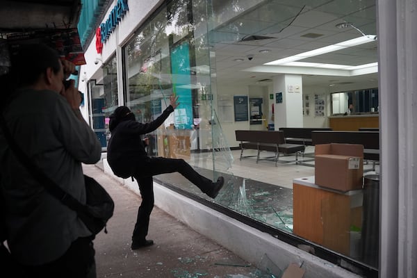 A demonstrator kicks in a bank storefront window at the end of peaceful protest that turned violent against gentrification, as the increase in remote workers has risen prices and increased housing demand in neighborhoods like Condesa and Roma, in Mexico City, Friday, July 4, 2025. (AP Photo/Aurea Del Rosario)