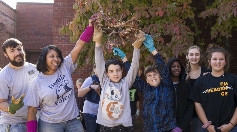 Dacula Middle School teacher of the year Derek Tuthill (far left) and Dacula Middle School principal Kimberly Bussey (second from left) pose for a photo with students after extracting a root from the ground during a school beautification event at Dacula Middle School, Friday, Oct. 19, 2018. Students, faculty, volunteers and parents planted plants, decorated plant pots and cleaned up a courtyard at the school. (ALYSSA POINTER/ALYSSA.POINTER@AJC.COM)