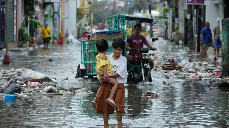 A woman and child crosses a flooded street due to Typhoon Fung-wong and high tide on Monday, Nov. 10, 2025, in Navotas, Philippines. (AP Photo/Aaron Favila)
