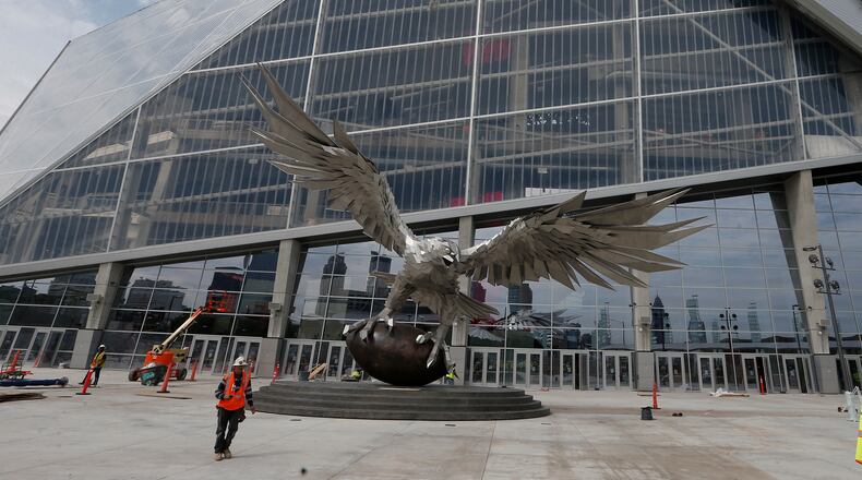 A man walks past a sculpture of a Falcon outside the entrance to Mercedes Benz Stadium, the new home of the Atlanta Falcons football team and the Atlanta United soccer team, Tuesday, July 25, 2017, in Atlanta. (AP Photo/John Bazemore)