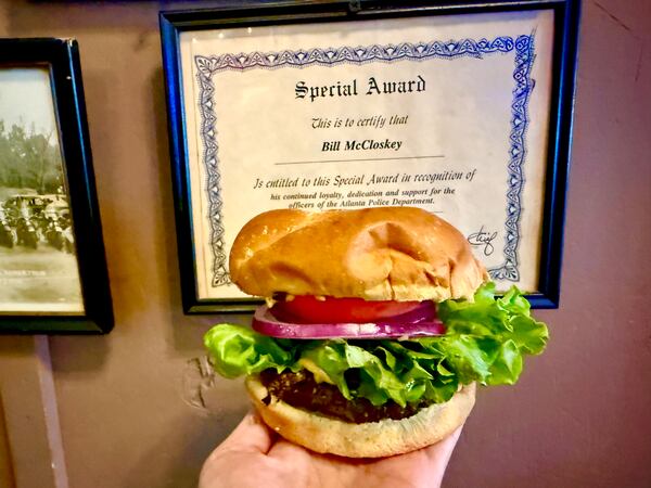A hand holds a loaded burger in front of a "Special Award" recognizing Bill McCloskey.