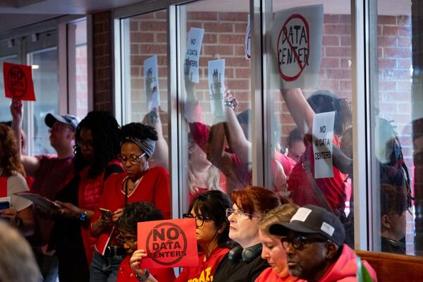 Data center opponents hold signs against a window to the Marietta City Council chambers during a meeting with an overflow crowd Wednesday, June 10, 2026. (Ben Gray for the AJC)
