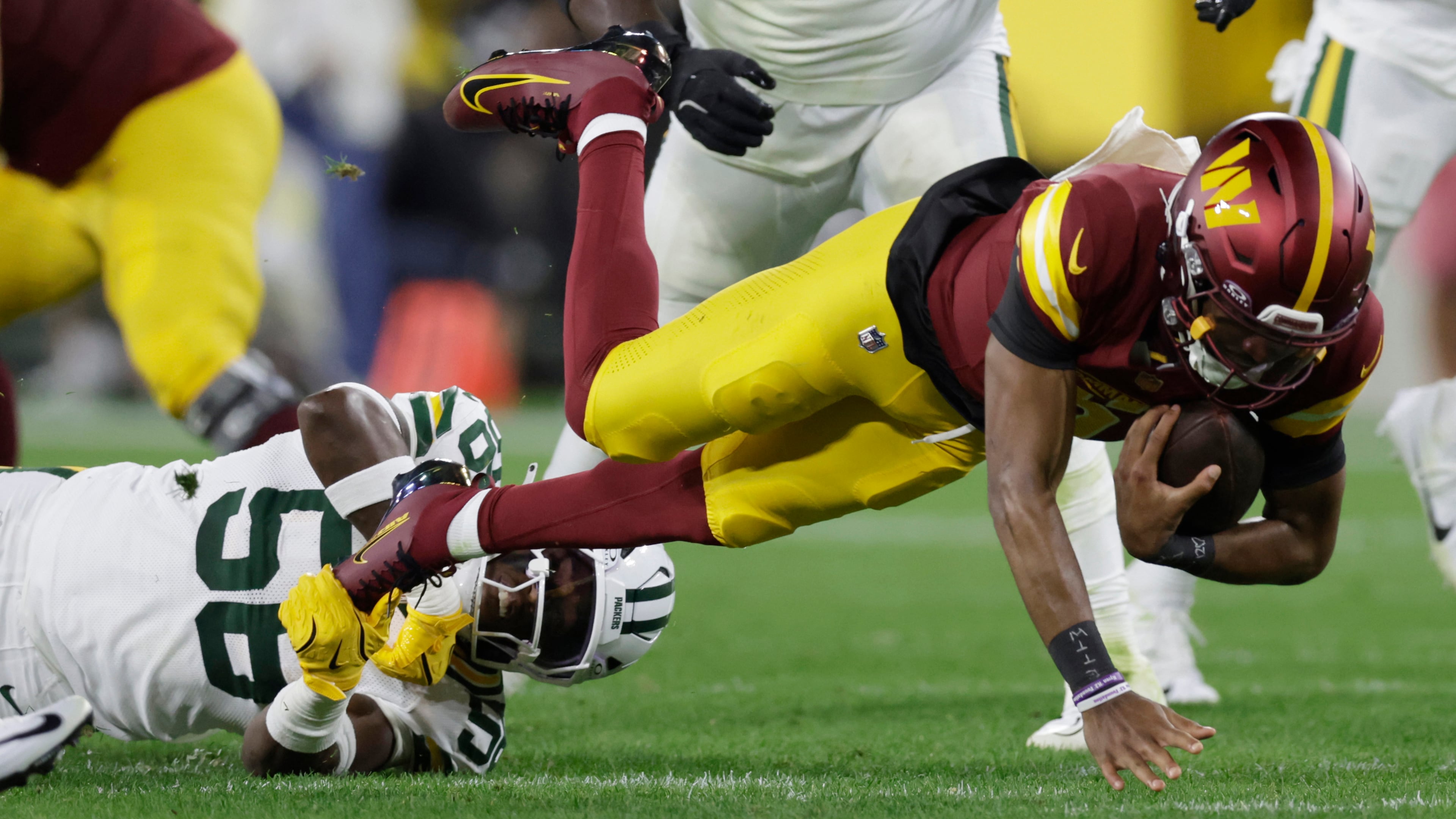 Washington Commanders quarterback Jayden Daniels, right, struggles for yardage as Green Bay Packers linebacker Isaiah McDuffie (58) defends during the first half of an NFL football game Thursday, Sept. 11, 2025, in Green Bay, Wis. (AP Photo/Matt Ludtke)