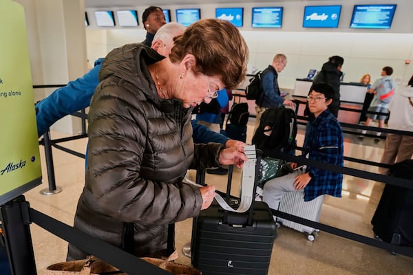 A woman checks her baggage tag as she waits in line at the Alaska Airlines counter, at Newark Liberty International Airport, in New Jersey, Friday, May 23, 2025. (AP Photo/Richard Drew)