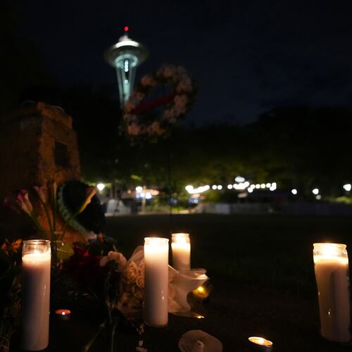 Flowers and candles are seen placed with the Space Needle at background, during the vigil for victims the day after a shooting at Seattle Center during the Bite of Seattle food festival, Monday, July 27, 2026, in Seattle. (AP Photo/Lindsey Wasson)