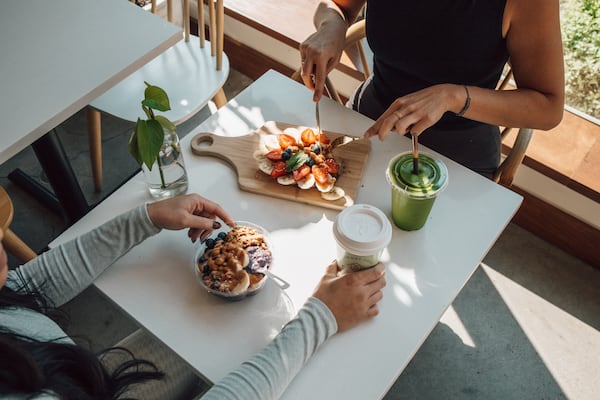 Two people sit at a table at Toastique with food and drink items between them.