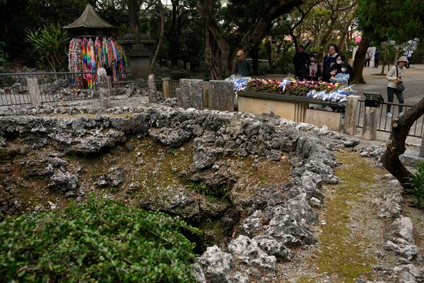 Visitors bring flowers and pray at the "Himeyuri" cenotaph, not seen, created by a cave in Itoman, on the main island of the Okinawa archipelago, southern Japan, Friday, Feb. 14, 2025, as they visit the Himeyuri peace museum that commemorates the Himeyuri female student corps who died during the Battle of Okinawa towards the end of the World War II in 1945. (AP Photo/Hiro Komae)