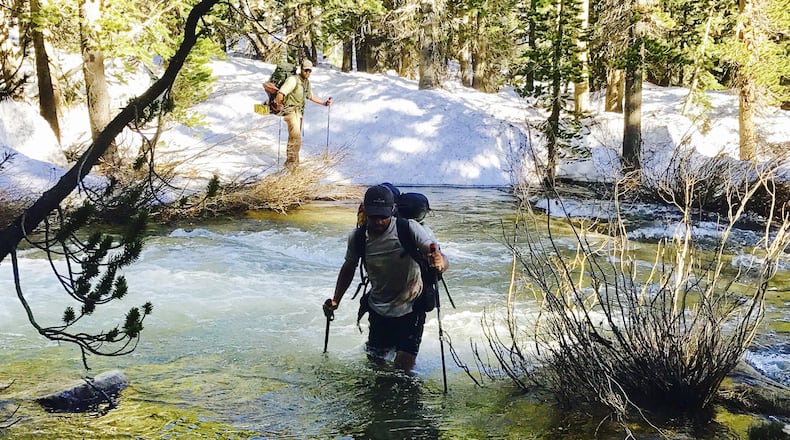 In this Tuesday, June 6, 2017, photo, Jake Gustafson crosses a creek along the Pacific Crest Trail near Kings Canyon National Park, Calif. Jake Gustafson, 21, a McDonald's manager from Pennsylvania, was one of those pressing on despite what he called "fear mongering" on social media. The worst thing he encountered as he and a friend approached Yosemite this week was sunburned nostrils from solar reflection off snow. "We're considered the daredevils," said Gustafson, who sends a "Not dead yet" message by satellite to his mother each night. "We like the sense of danger, I guess." (Wesley Tils via AP)