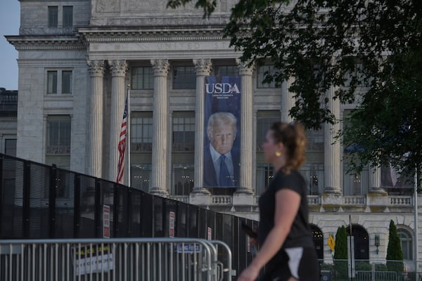 A woman walks past security fencing set up on the National Mall, during preparations for an upcoming military parade commemorating the Army's 250th anniversary and coinciding with President Donald Trump's 79th birthday, Thursday, June 12, 2025, in Washington. (AP Photo/Rod Lamkey, Jr.)