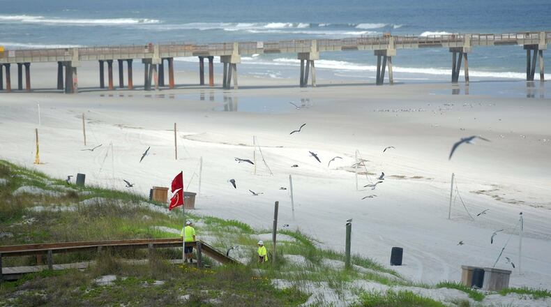 In this March 23, 2020 photo, workers take advantage of the lack of beachgoers to do some repairs to the dune walkover bridges along Jacksonville Beach in Jacksonville, Fla. Mayor Lenny Curry says Duval County beaches are reopening Friday, April 17, 2020, with restricted hours, and they can be used only for walking, biking, hiking, fishing, running, swimming and surfing. (Bob Self/The Florida Times-Union via AP)