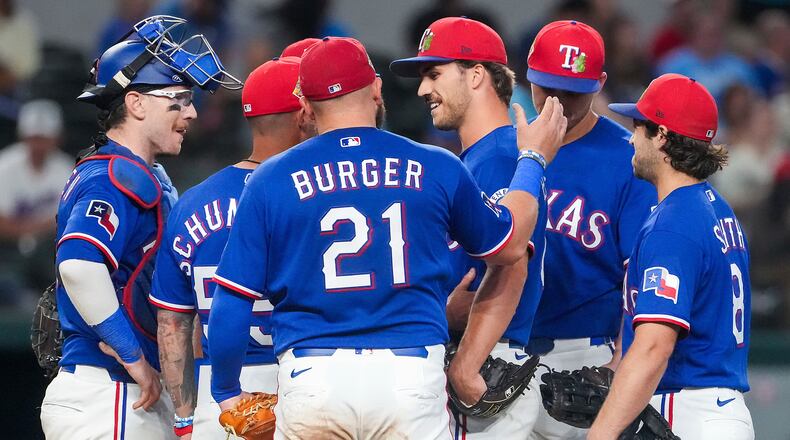 Texas Rangers pitcher Carter Baumler, third from right,gets a pat on the back from first baseman Jake Burger (21) as he gets a visit at the mound from manager Skip Schumaker, second from left, to inform him he has made the opening day roster during the fifth inning of an exhibition baseball game against the Kansas City Royals, Monday, March 23, 2026, in Arlington, Texas. (Smiley N. Pool/The Dallas Morning News via AP)