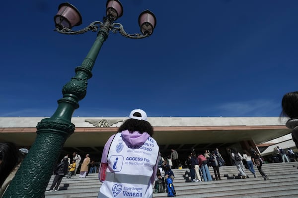 Stewards check tourists' QR codes outside the main train station in Venice, Italy, Friday, April 18, 2025, as the city for a second year is charging day-trippers an arrivals tax. (AP Photo/Antonio Calanni)