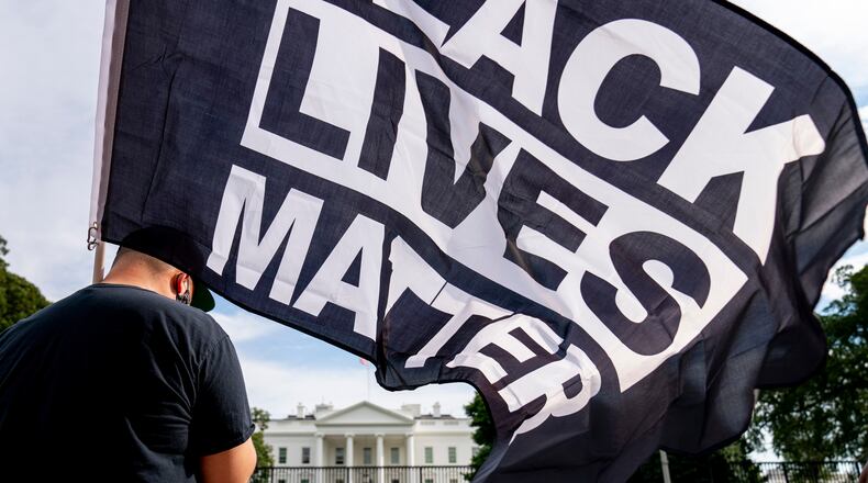 FILE - A man carries a Black Lives Matter flag in Lafayette Square outside the White House on the fourth night of the Republican National Convention, Aug. 27, 2020, in Washington. (AP Photo/Andrew Harnik, File)