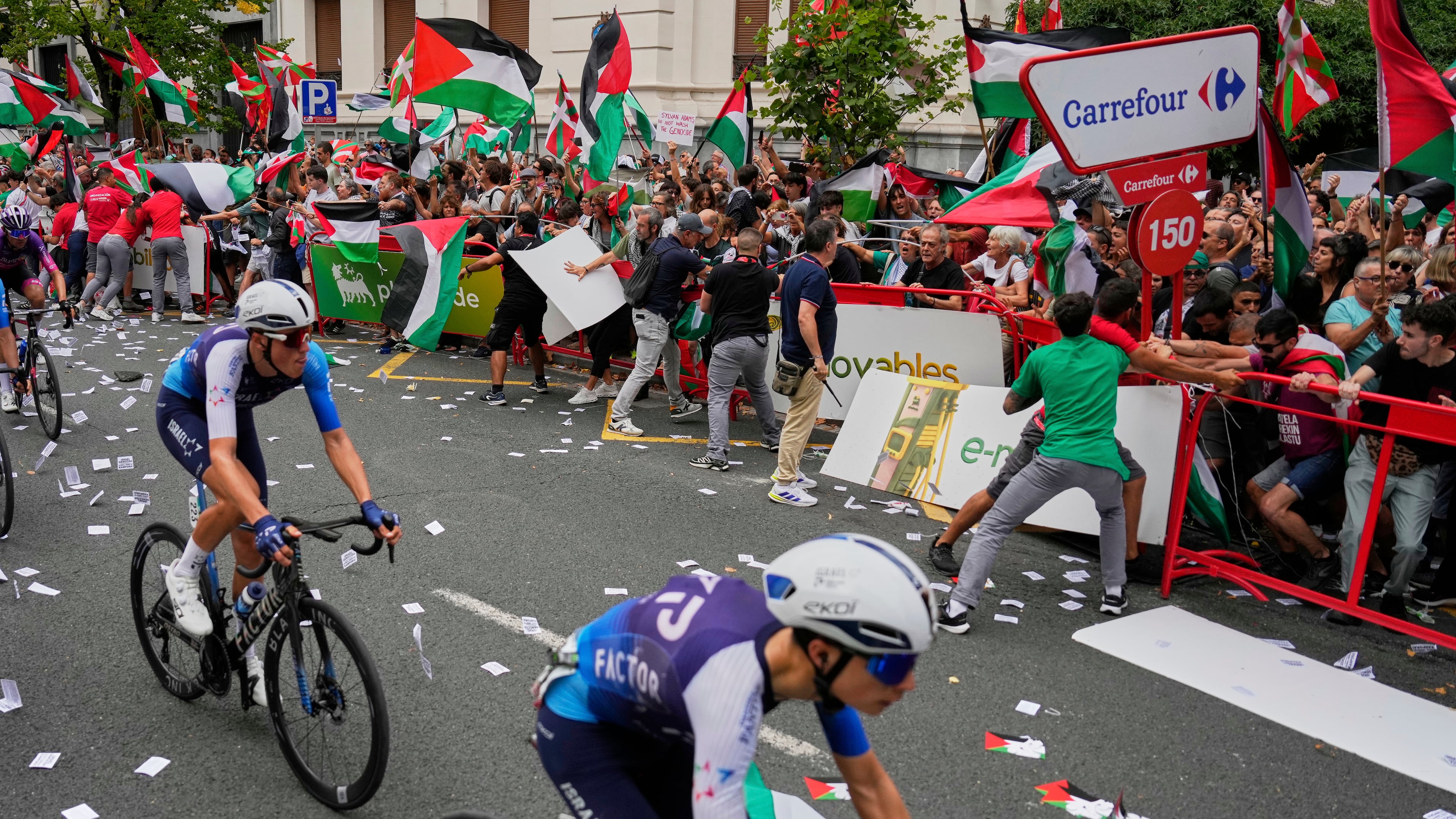 Riders of the Israel Premier Tech team compete as people holding Palestinian flags try to disrupt the eleventh stage of the Spanish Vuelta cycling race, from Bilbao to Bilbao, Spain, Wednesday, Sept. 3, 2025. (AP Photo/Miguel Oses)