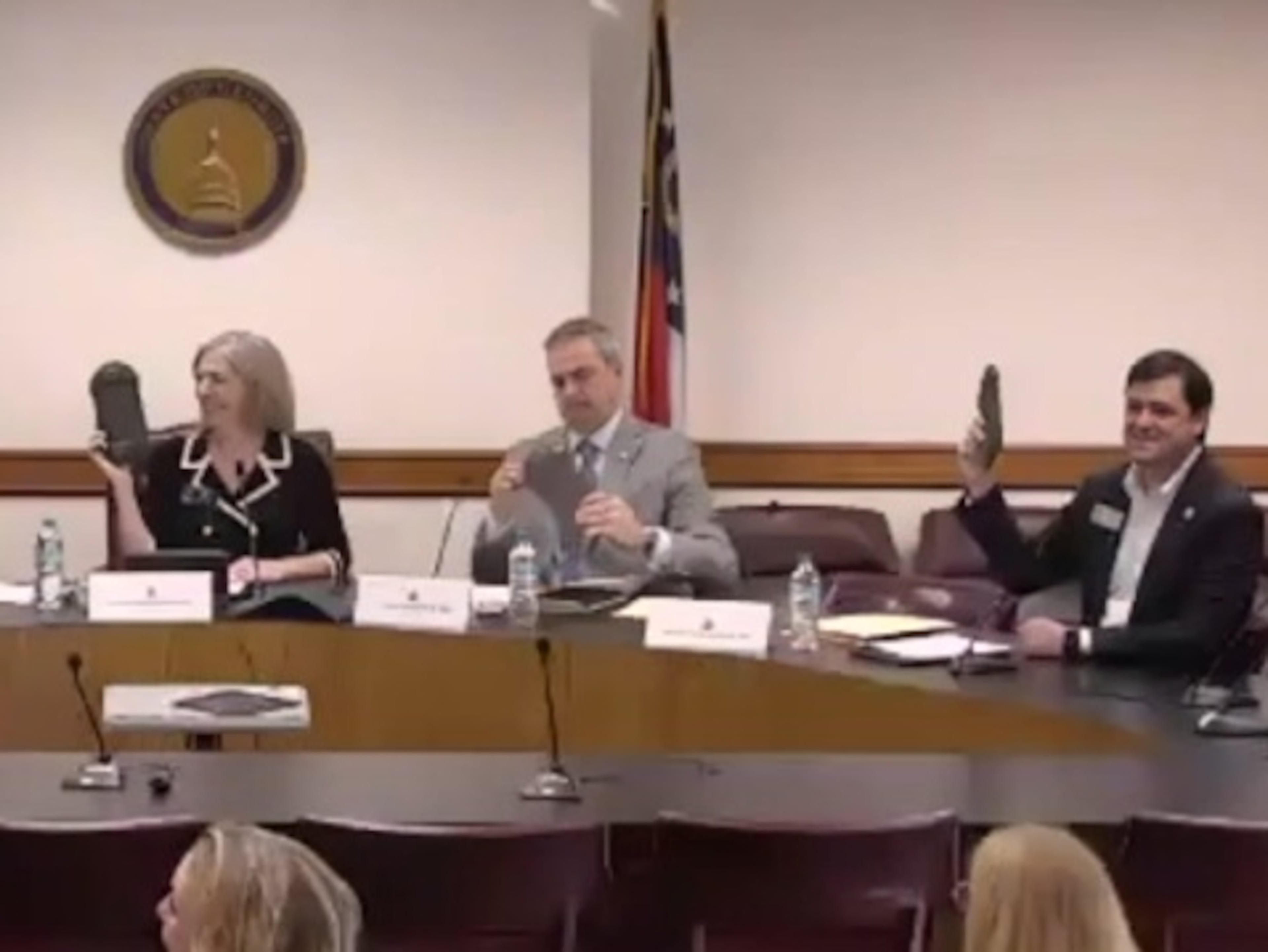 Members of a Georgia Senate study committee, including (left to right) Sens. Sally Harrell, Shawn Still and Scott Hilton, displayed locked pouches containing their cellphones during a hearing on Wednesday. (Screenshot)
